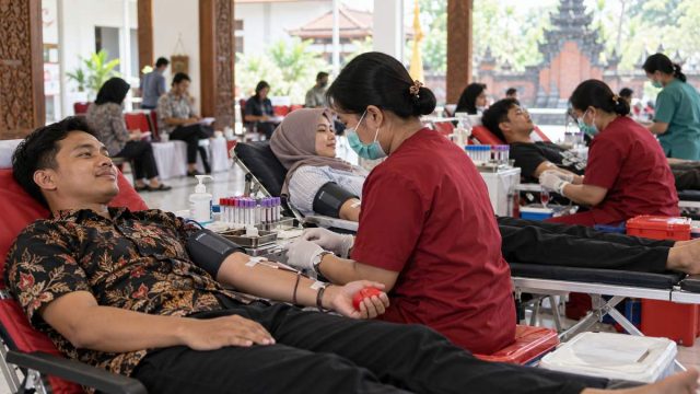 Petugas kesehatan ilustratif membantu donor darah sukarela di ruang layanan.