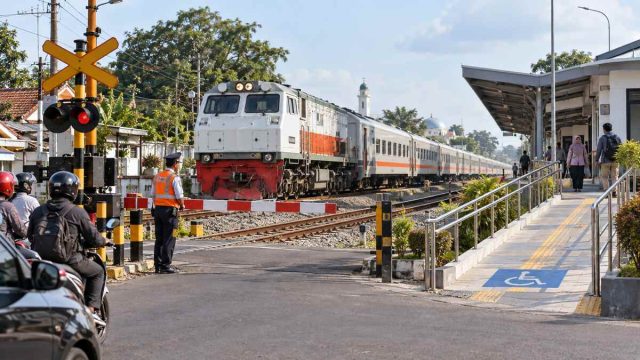 Kereta melintas di perlintasan berpagar dekat stasiun dengan jalur landai bagi pengguna kursi roda