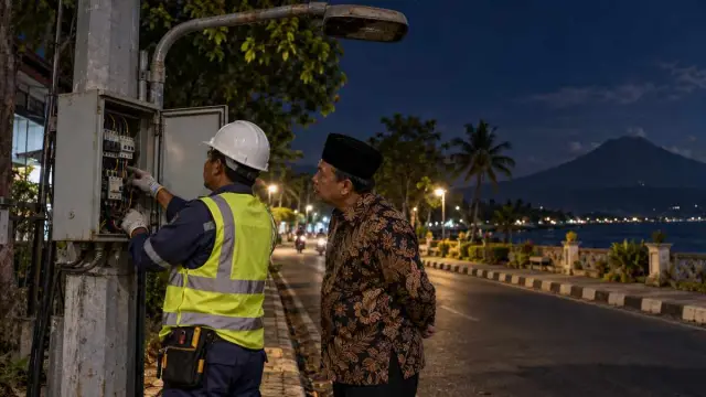Petugas memeriksa panel lampu jalan ditemani legislator pada malam hari di Situbondo