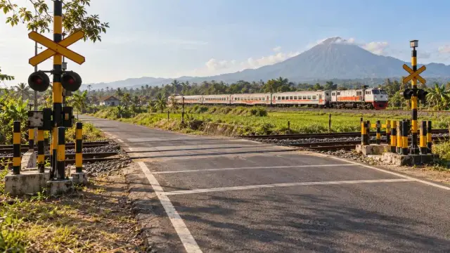 Perlintasan kereta di jalan desa terlihat dari kejauhan pada siang hari.