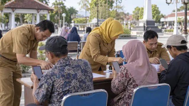 Petugas pelayanan membantu warga menggunakan ponsel di meja layanan terbuka.